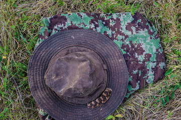 Hunting season concept: hunting hat with pheasant feather and camouflage clothing on the grass top view