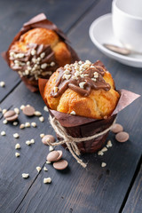 Homemade vanilla muffin with milk chocolate and nuts and a white cup on a wooden background. Close-up