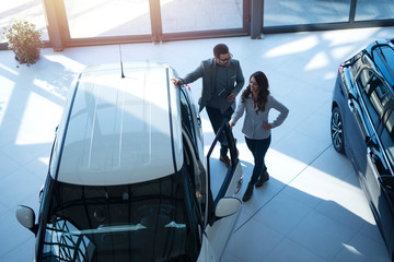 Top view of people looking at brand new car they want to buy at vehicle dealership.