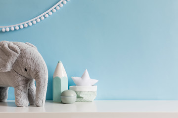 Cozy scandinavian newborn baby room with gray plush elephant ,white stars lamp and children accessories. Stylish interior with blue walls and haniging white garland. Template. Copy space.  - obrazy, fototapety, plakaty