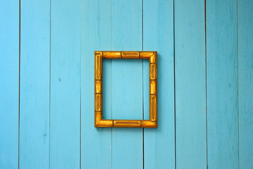 Fototapeta na wymiar On the blue plank wall in the center hangs an empty golden frame