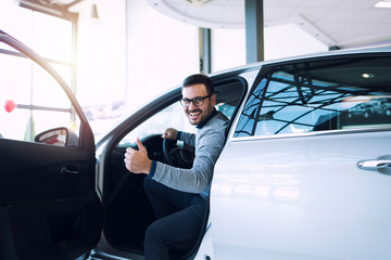 Happy satisfied customer just bought a brand new car at vehicle dealership. Car buyer sitting at...