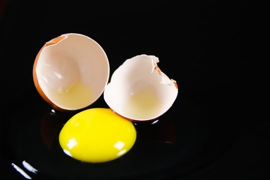 Close up of brown cracked egg shell with raw yellow yalk and slimy egg white on reflecting shiny smooth glass black background