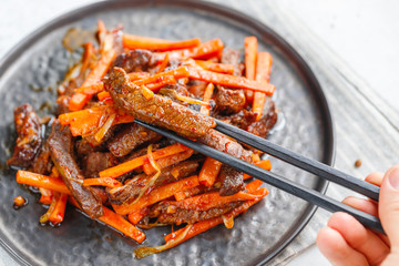 Close-up of Chinese spicy Szechuan beef meal on a black plate with wooden sticks over white table. Asian food recipe; portion for one person.