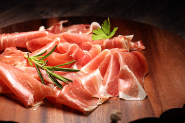 Italian prosciutto crudo or jamon with rosemary. Raw ham on wooden board