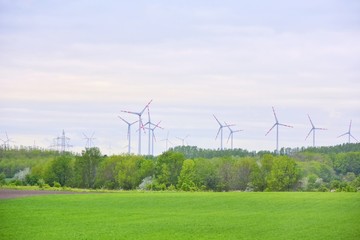 Wind mill turbines in field with blue sky and clouds and green summer grass on the front. Alternative renewable energies. Ecological clean energy. Electricity wind stations. Wind turbine generator 