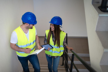 Industrial workers with hardhat and reflective jacket walking the stairs in factory discussing about work.