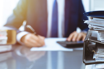 Binders with papers waiting to be processed with businessman or bookkeeper back in blur. Accounting planning budget. Audit, insurance  and business concept