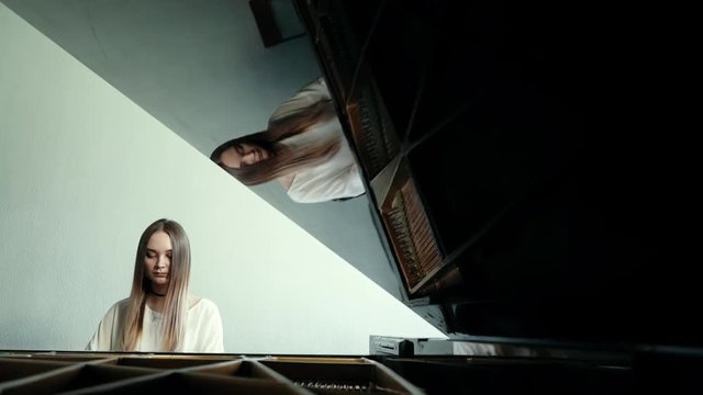Girl pianist with long hair plays gentle classical music on a grand piano on the background of a beautiful wall in slow motion. Student pianist preparing for classes in the classroom