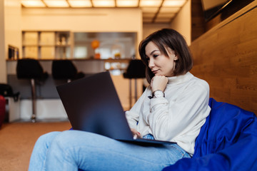 Happy pretty woman using laptop sitting on cosy sofa at home