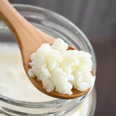Milk kefir grains on wooden spoon on top of a jar of kefir, photographed with natural light (Selective Focus, Focus in the middle of the kefir grains)