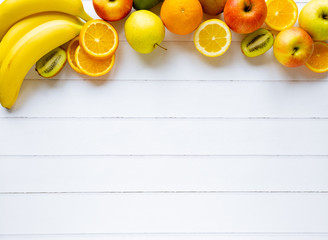 Colorful fresh summer fruits banana orange apple kiwi on white wooden background, healthy organic...