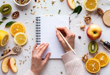 Female hand write in notebook on healthy food background, women diet nutrition recipe menu, fresh summer fruit granola seeds on white table organic super food, health care detox, top view, copy space - obrazy, fototapety, plakaty