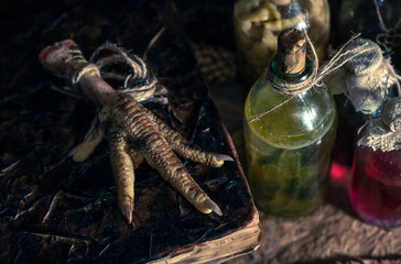 A witchery stuff: multiple tincture bottles, bunches of dry healthy herbs, stack of ancient ritual books, amulets, candles, chicken feet, sack of medicinal and magical herbs. 