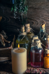 A witchery stuff: multiple tincture bottles, bunches of dry healthy herbs, stack of ancient ritual books, amulets, candles, chicken feet, sack of medicinal and magical herbs. 