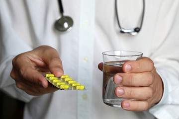Doctor holding blister pack of pills and glass of water, therapist giving medication in yellow...