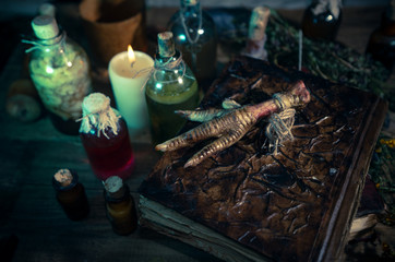 A witchery stuff: multiple tincture bottles, bunches of dry healthy herbs, stack of ancient ritual books, amulets, candles, chicken feet, sack of medicinal and magical herbs. 