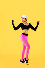 Sporty woman in fashionable sportswear does the exercises with dumbbells. Photo of muscular woman on yellow background. Strength and motivation.