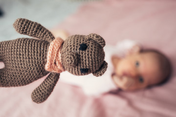 3)	The little girl in pink clothes lies on a pink background. Next to the little girl is a brown knitted bear