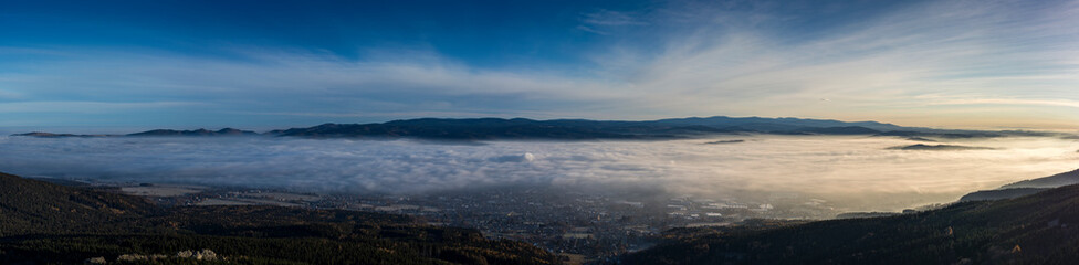 Landscape with inverse cloudiness and protruding peaks of mountains during sunrise.