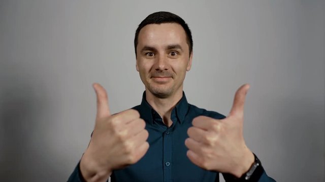 Closeup portrait of a young business man emotionally showing gesture double thumbs up and looking at camera on a white background. Charismatic actor play concept of emotions