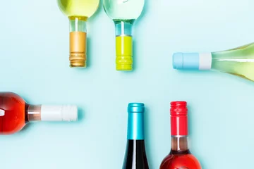 Foto op Plexiglas Layout frame of foil caps in different bright colors of white and rose wine bottles on blue background with copy space. Minimal abstract colorful mockup concept of alcohol beverage. Flat lay. © PINKASEVICH