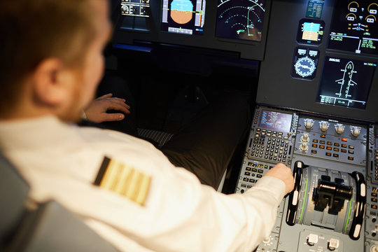 Close-up of airline pilot in uniform sitting at control panel of aircraft cockpit and checking setups while preparing for flight