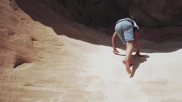 Attractive young boy climbing up big dragon rock in desert 4k