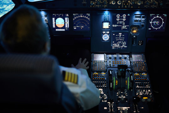 Rear View Of Unrecognizable Pilot Sitting At Control Panel With Radar Devices And Flight System Buttons And Flying Plane On Autopilot