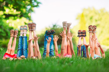 Children lying on green grass in park on a summer day with their legs lifted up to the sky.
