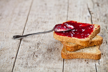 Toasted cereal bread slices with homemade cherry jam and spoon closeup on rustic wooden table...