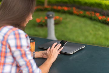 Attractive young woman reading a text message on her cell phone. Girl sitting outdoors using smartphone