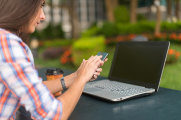 Attractive young woman reading a text message on her cell phone. Girl sitting outdoors using smartphone