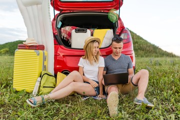 Young couple sitting on the lawn working at a laptop remotely relaxing at a camping in the summer Sunny day earning online