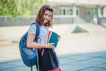 A girl holding two books red and green and smiling. Schoolgirl on the background of the school after the summer holidays. Ready to start the school year schoolgirl.