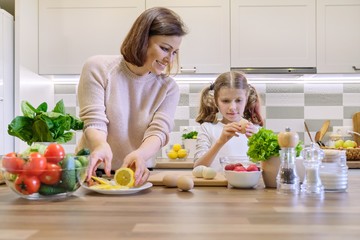 Smiling mother and daughter 8, 9 years old cooking together in kitchen vegetable salad. Healthy home food, communication parent and child.