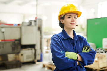Waist up portrait of confident female worker wearing hardhat looking at camera while posing at factory, copy space