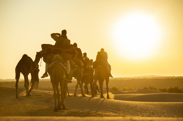 Stunning view of some tourists riding camels on the dunes of the Thar Desert in Rajasthan during a beautiful sunset. India. The Thar Desert is a large arid region in the northwestern part of India.