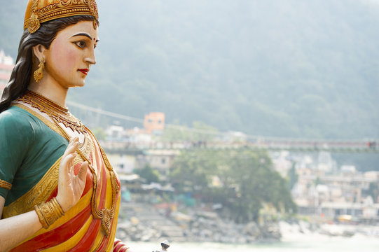 Close-up view of the statue of sitting Goddess Parvati on the riverbank of the Ganges river. Blurred Lakshman Jhula bridge in the background. Rishikesh, Uttarakhand, India.
