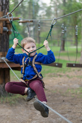 A little boy is training in a rope park. The child climbs the obstacle course. Active recreation in the park in the fresh air.