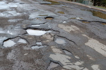 A paved road filled with many large potholes, the potholes are filled with water.