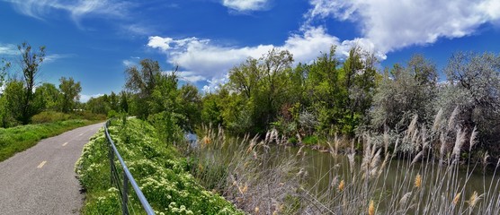 Jordan River Parkway Trail, Redwood Trailhead bordering the Legacy Parkway Trail, panorama views with surrounding trees and silt filled muddy water along the Rocky Mountains, Salt Lake City, Utah. 