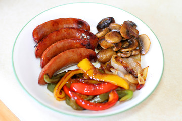 Plate of sausage with grilled bell peppers, mushrooms, and onion.