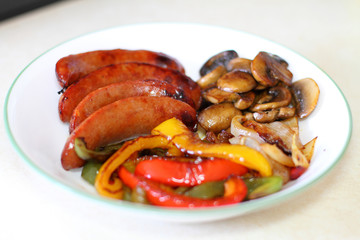 Plate of sausage with grilled bell peppers, mushrooms, and onion.