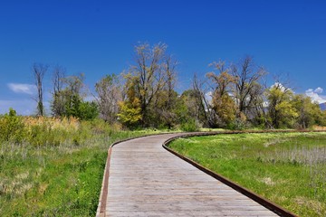 Jordan River Parkway Trail, Redwood Trailhead bordering the Legacy Parkway Trail, panorama views with surrounding trees and silt filled muddy water along the Rocky Mountains, Salt Lake City, Utah. 