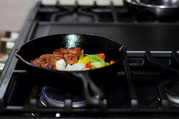 Sausage cooking on the stove in a cast iron skillet with bell peppers and onion.