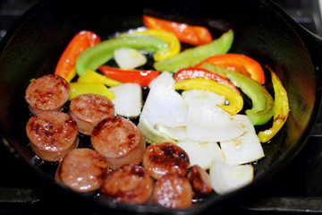 Sausage cooking on the stove in a cast iron skillet with bell peppers and onion.