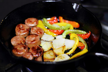 Sausage cooking on the stove in a cast iron skillet with bell peppers and onion.