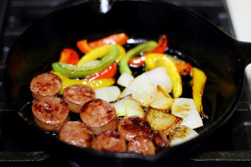 Sausage cooking on the stove in a cast iron skillet with bell peppers and onion.