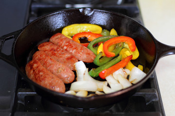 Sausage cooking on the stove in a cast iron skillet with bell peppers and onion.
